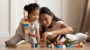Involved little daughter her vietnamese mother play on warm floor using wooden colorful blocks create towers and buildings improve fine motor skill of kid. Funny educational games for children concept